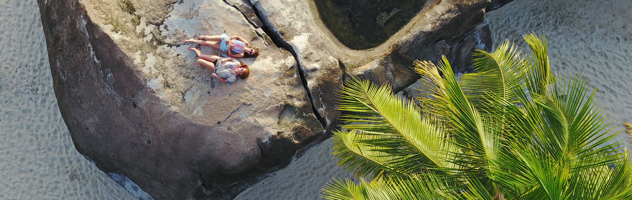 kids laying on a rock in the ocean outside batu villa with palm tree